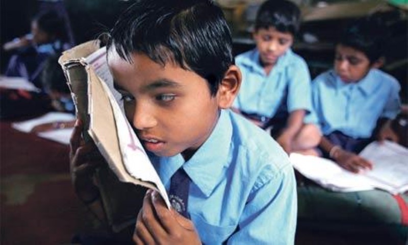 a child with low vision reading a book by bringing it closer to his eyes.