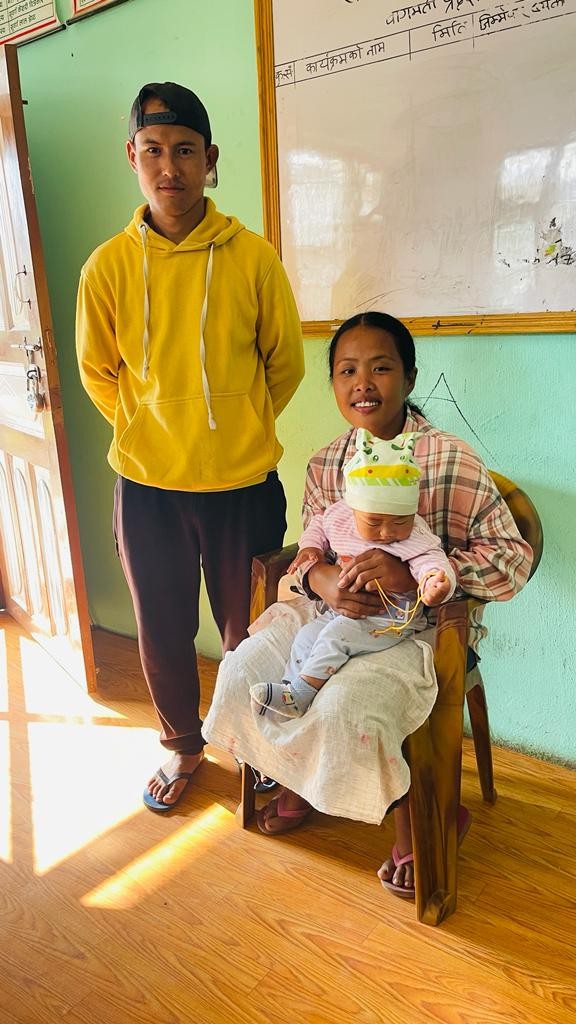 Women holding baby and man standing by side.